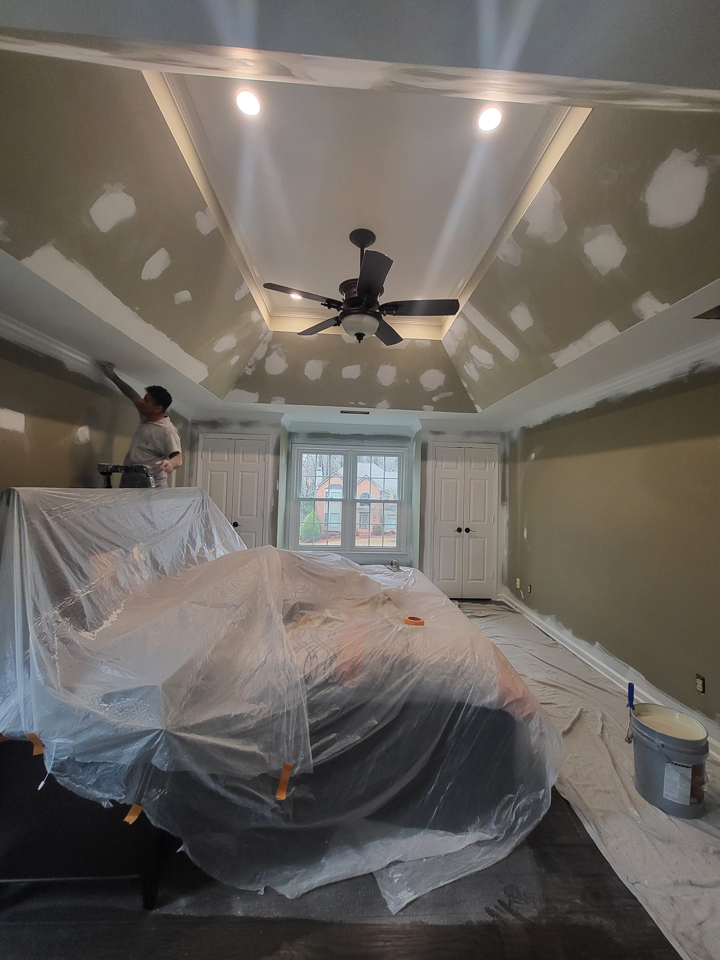 Bedroom mid-project — drywall patches sanded, furniture wrapped in plastic, ready for primer